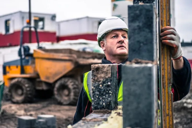 Construction worker with helmet and high-visibility vest laying bricks on a building site