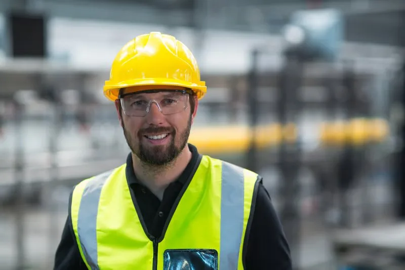Production worker with helmet, safety glasses and high-visibility vest in a factory hall