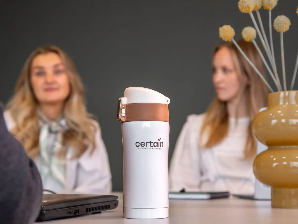 Termokopp med Certain-logo på et møtebord, med rådgivere i samtale i bakgrunnen